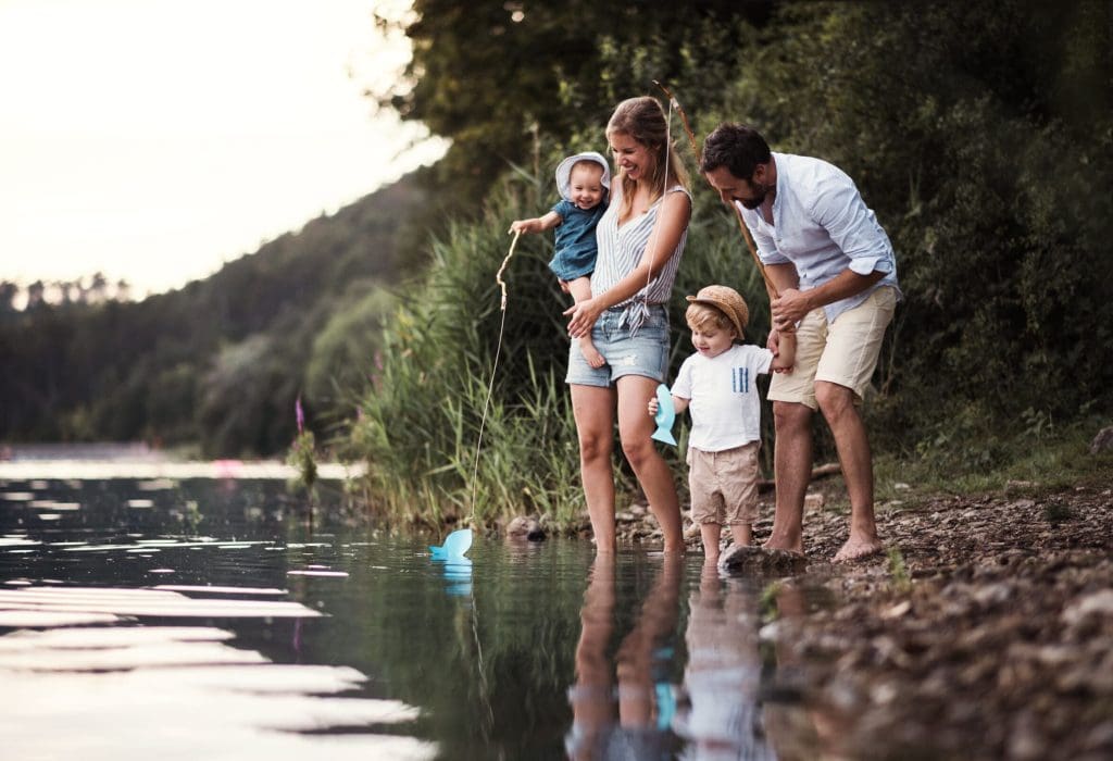 A young family with two toddler children outdoors by the river in summer. A young family with two toddler children spending time outdoors by the river in summer.
